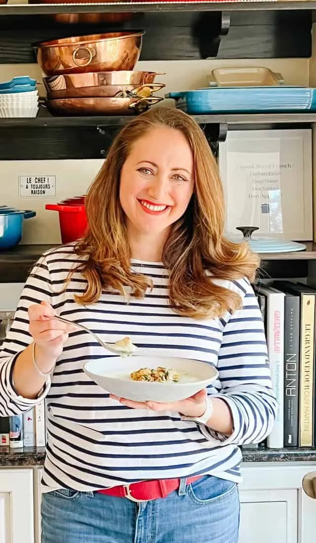 Anina Giannini in a Breton stripe shirt holding a finished dish in her kitchen
