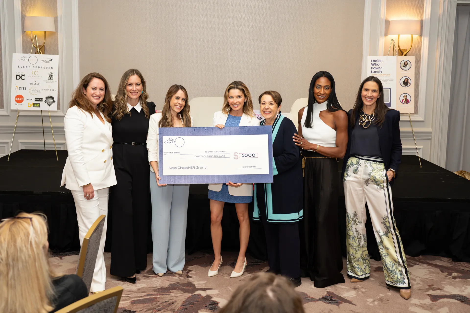 The Next ChaptHER co-founders presenting a $1,000 grant check to a recipient at a foundation event